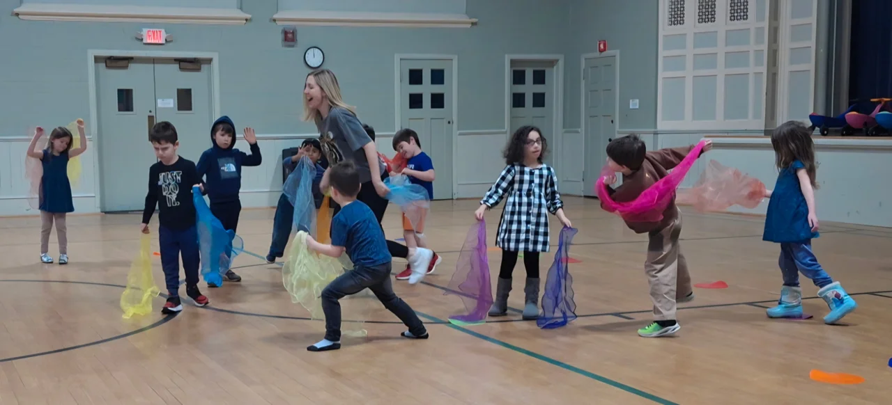 Children dancing with colorful scarves in a gym during a Dance Jam class